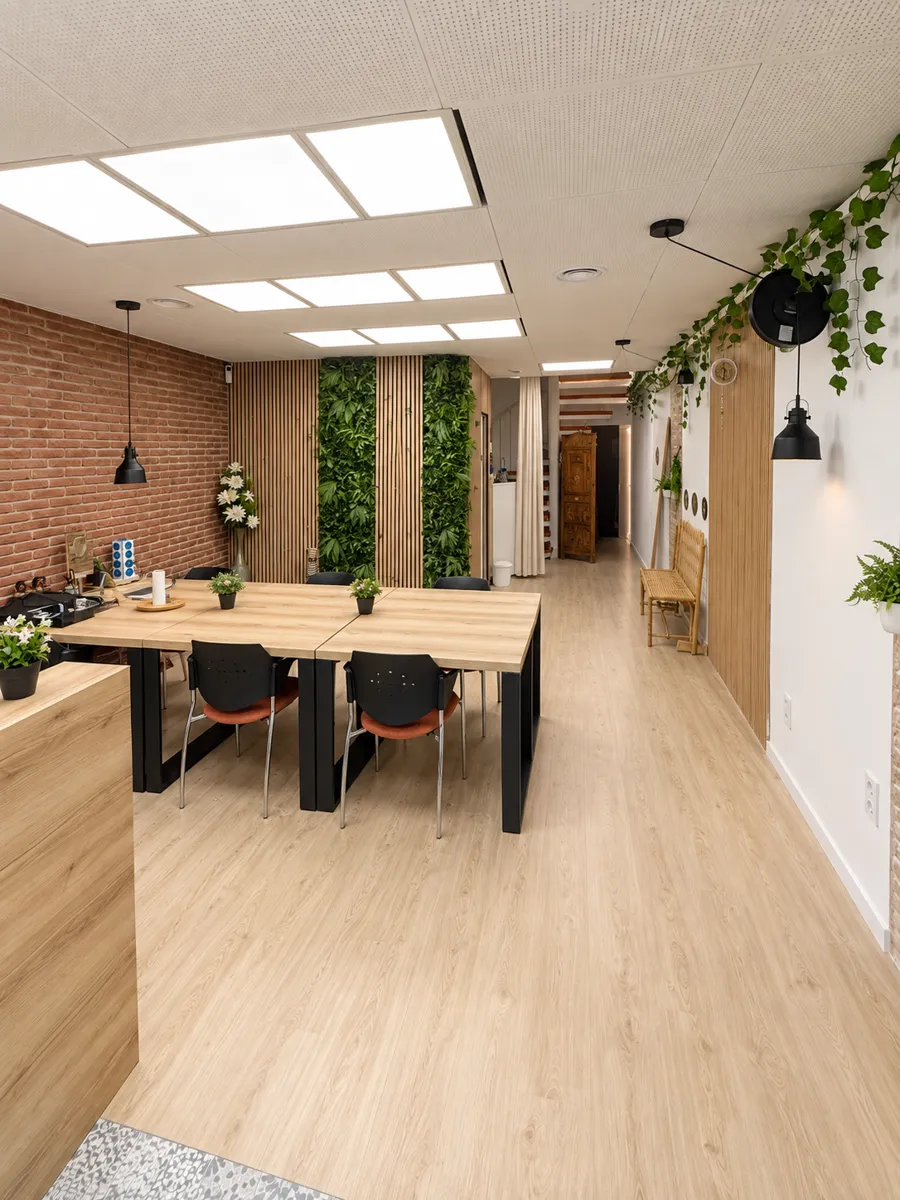 Zona de coworking amb taules de fusta, paret de maó i plantes